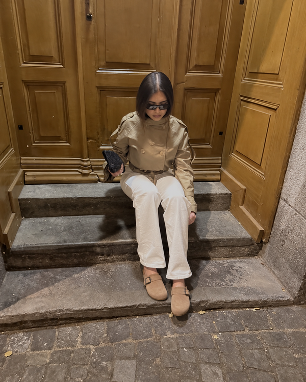 Tan Ashton clogs styled with a trench coat and white trousers on stone steps