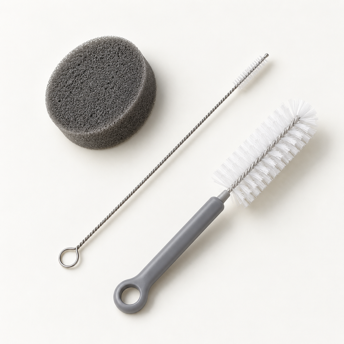 Cleaning Kit with a round gray sponge and two white-bristle cleaning brushes on an off-white studio background.