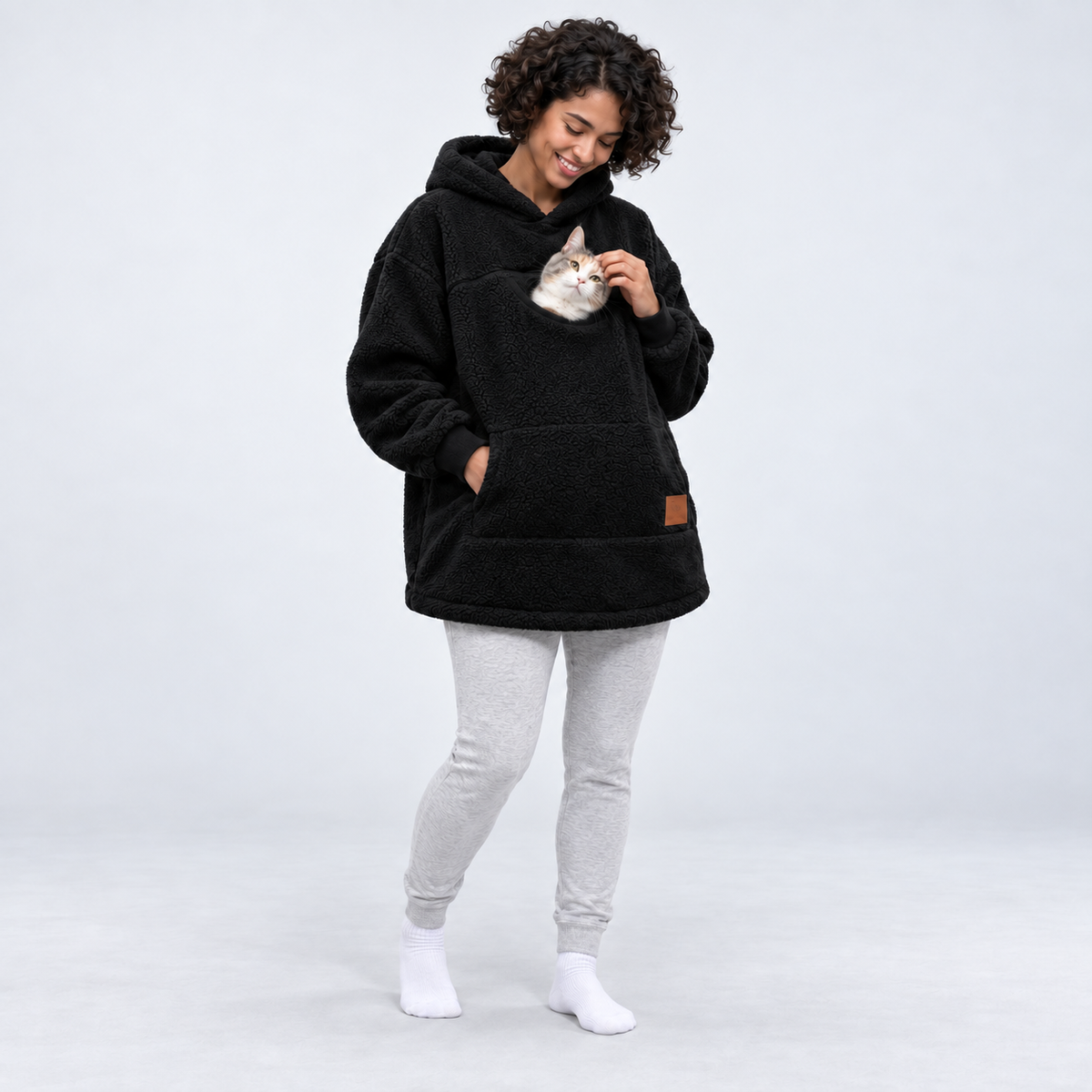 Black color: woman wearing the sherpa pet carrier hoodie with a cat in its front pouch.